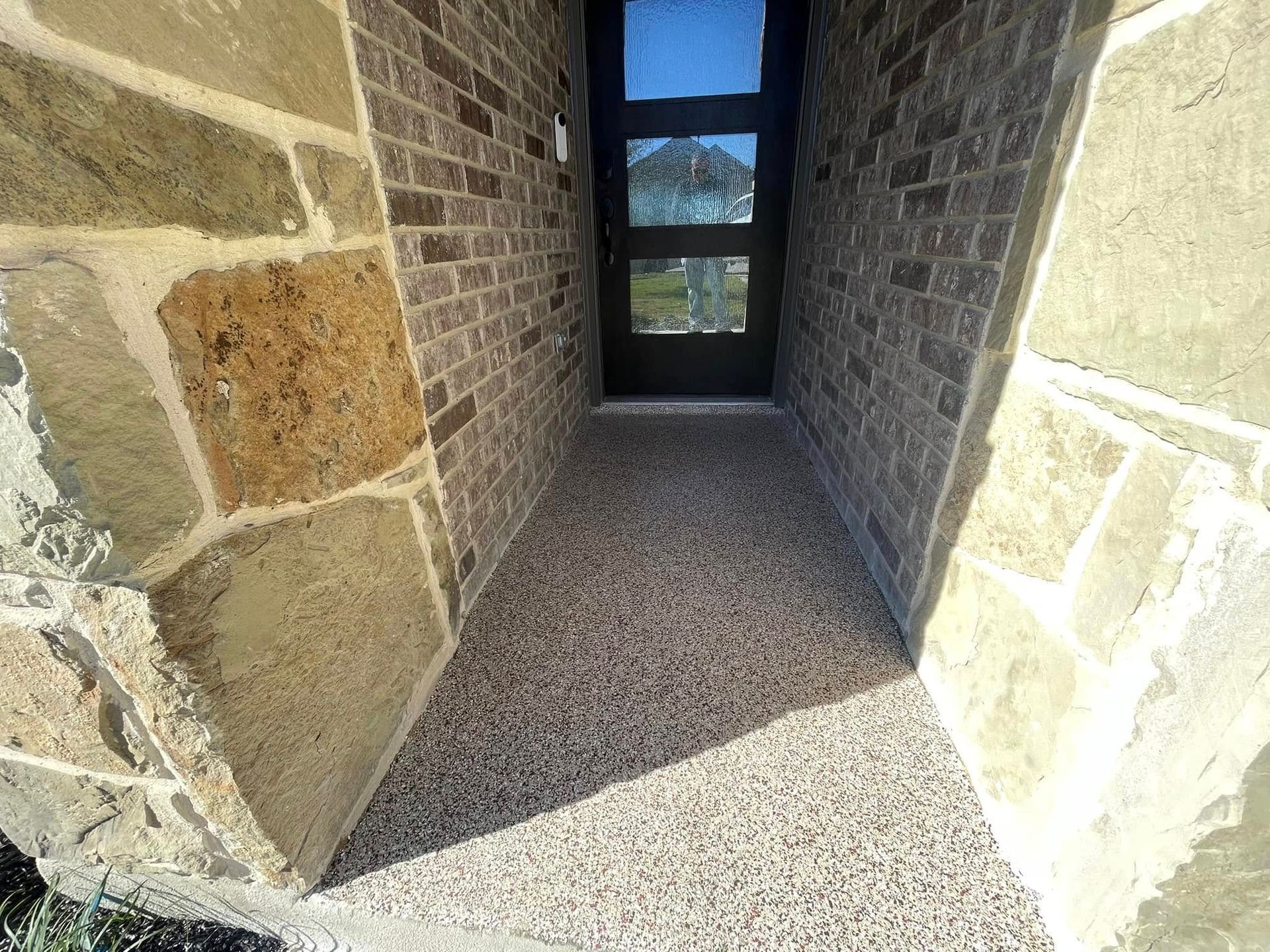 Entryway with gravel flooring, brick and stone walls, dark door with window.