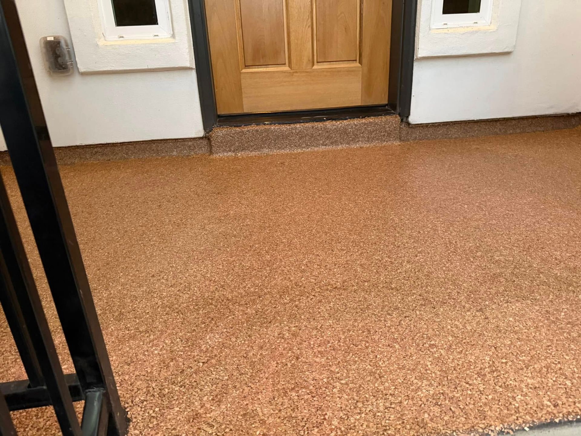 Beige speckled epoxy floor leads to a wooden door under a white porch.
