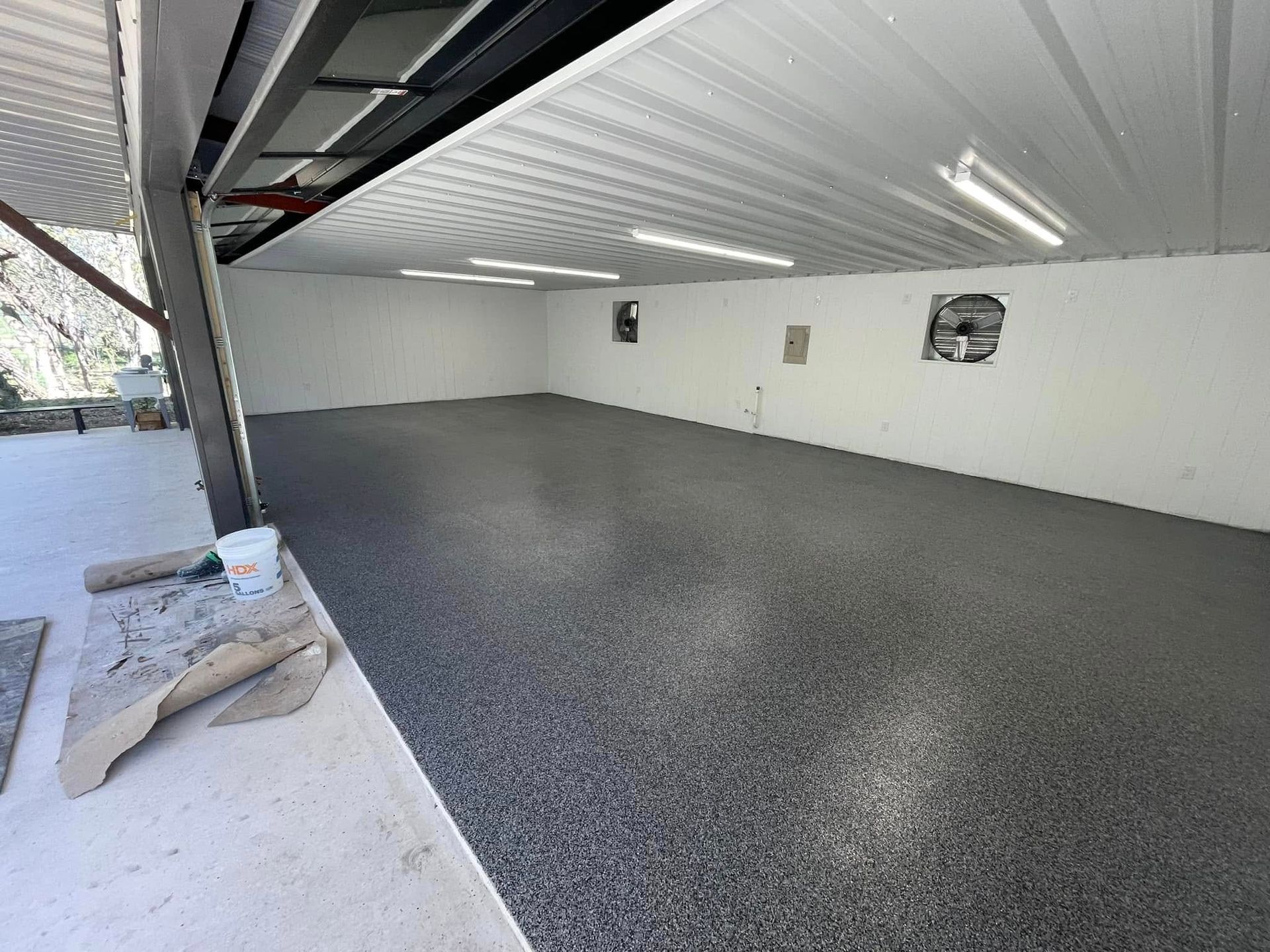 Garage interior with a gray epoxy floor and overhead lighting, open door to the left, white walls.