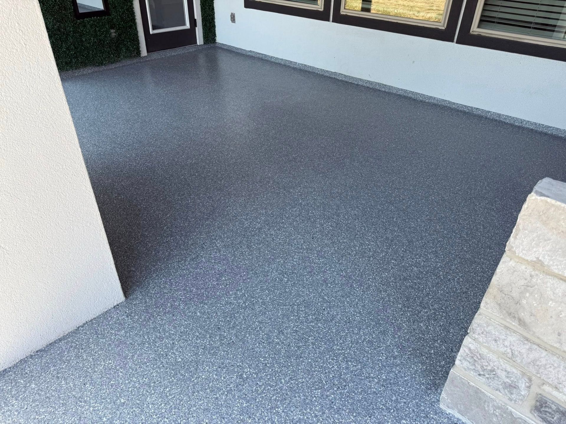 Gray speckled epoxy flooring on an outdoor patio, near a wall and windows.