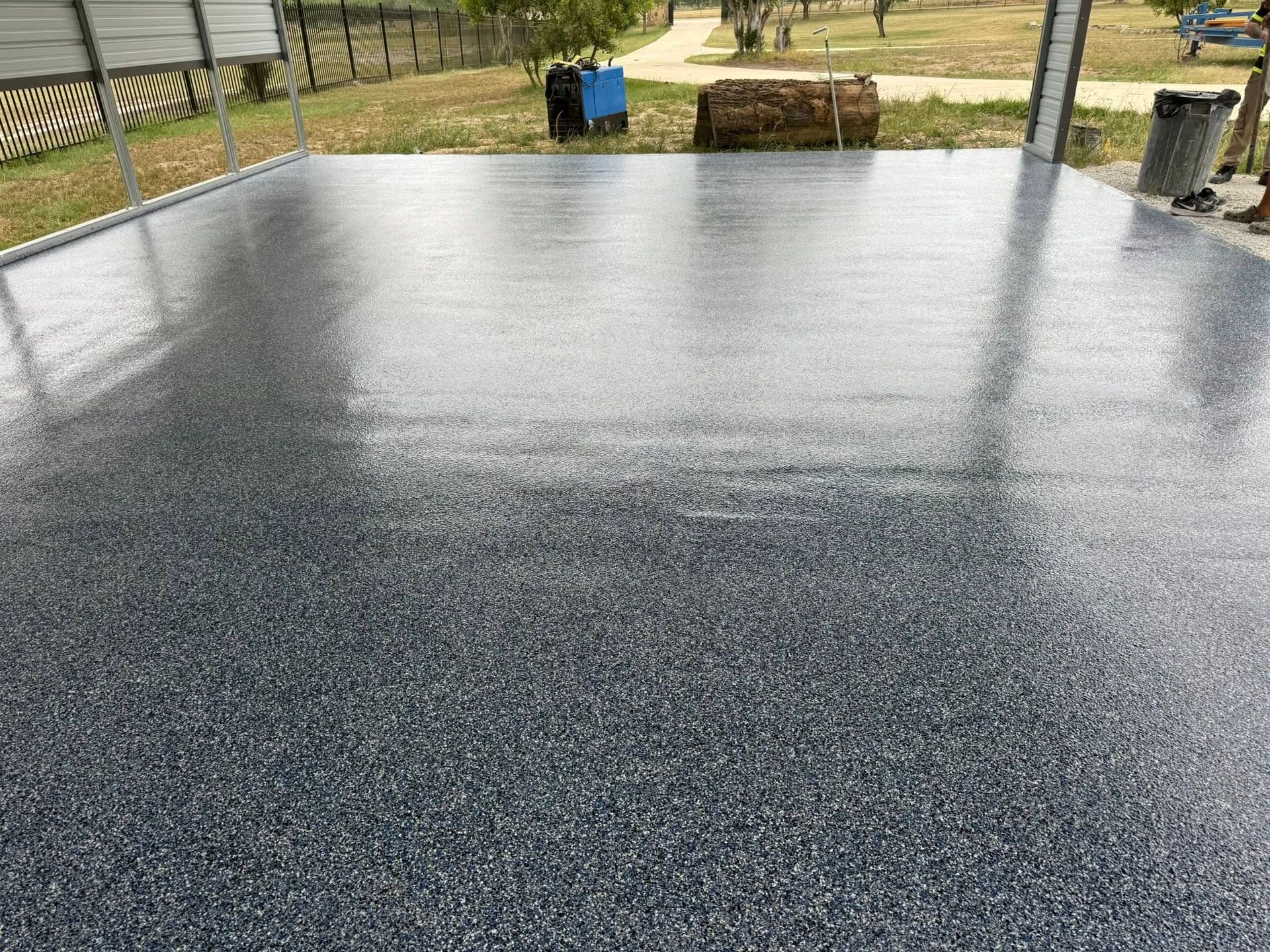 Gray speckled epoxy-coated concrete floor under a carport; outdoors with objects in the background.