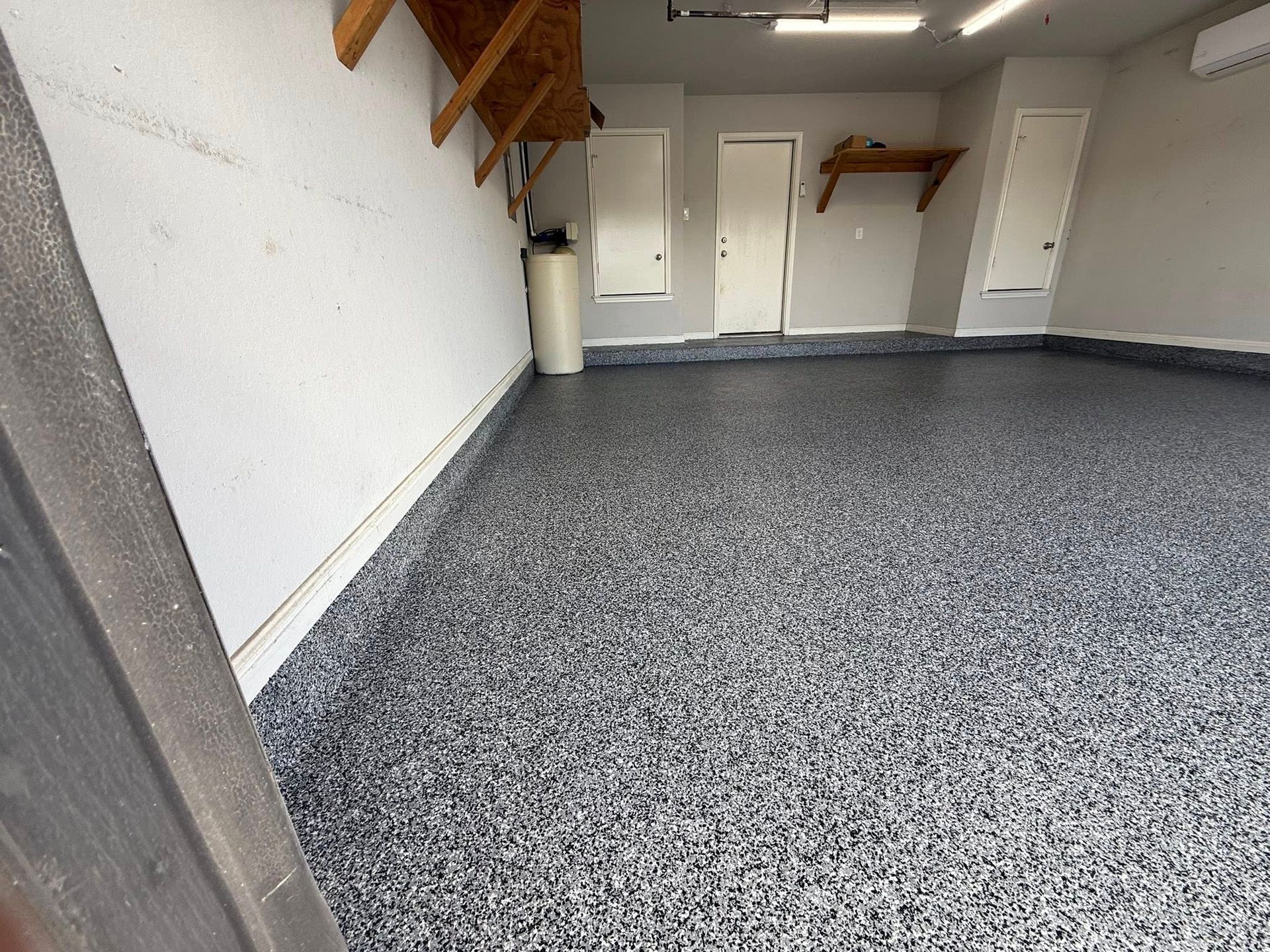 Garage with gray speckled epoxy floor, white walls, and two white doors.