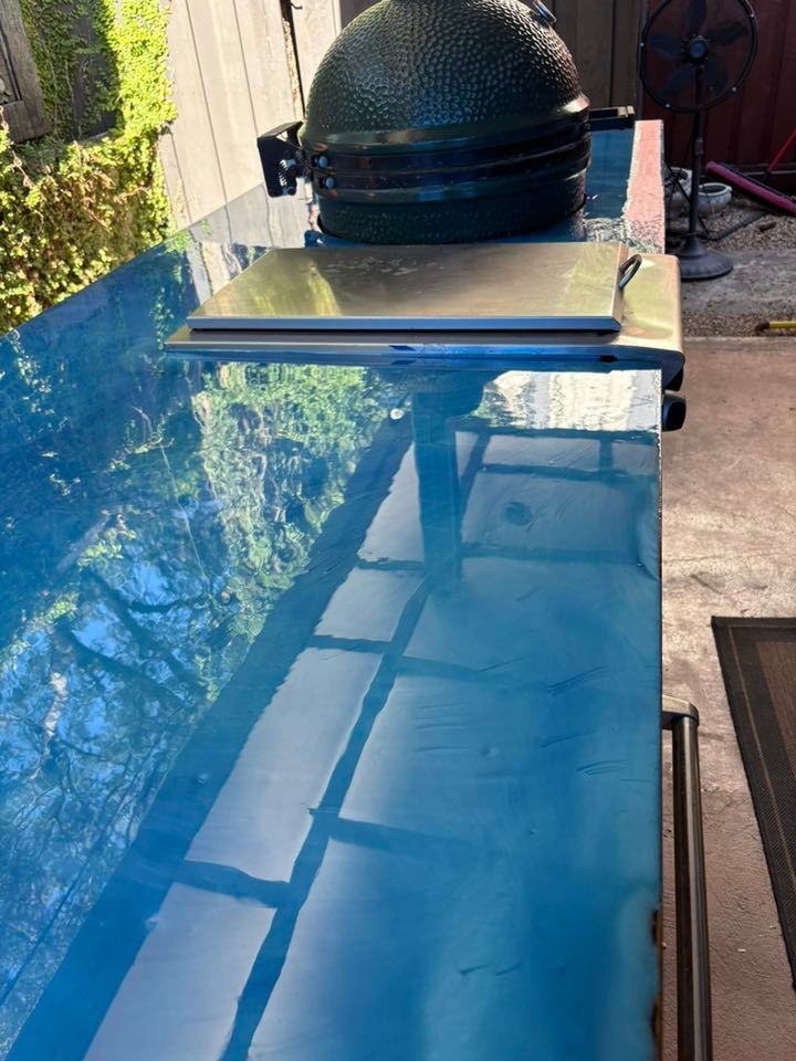Blue epoxy countertop with Big Green Egg grill, stainless steel shelf. Outdoor setting.