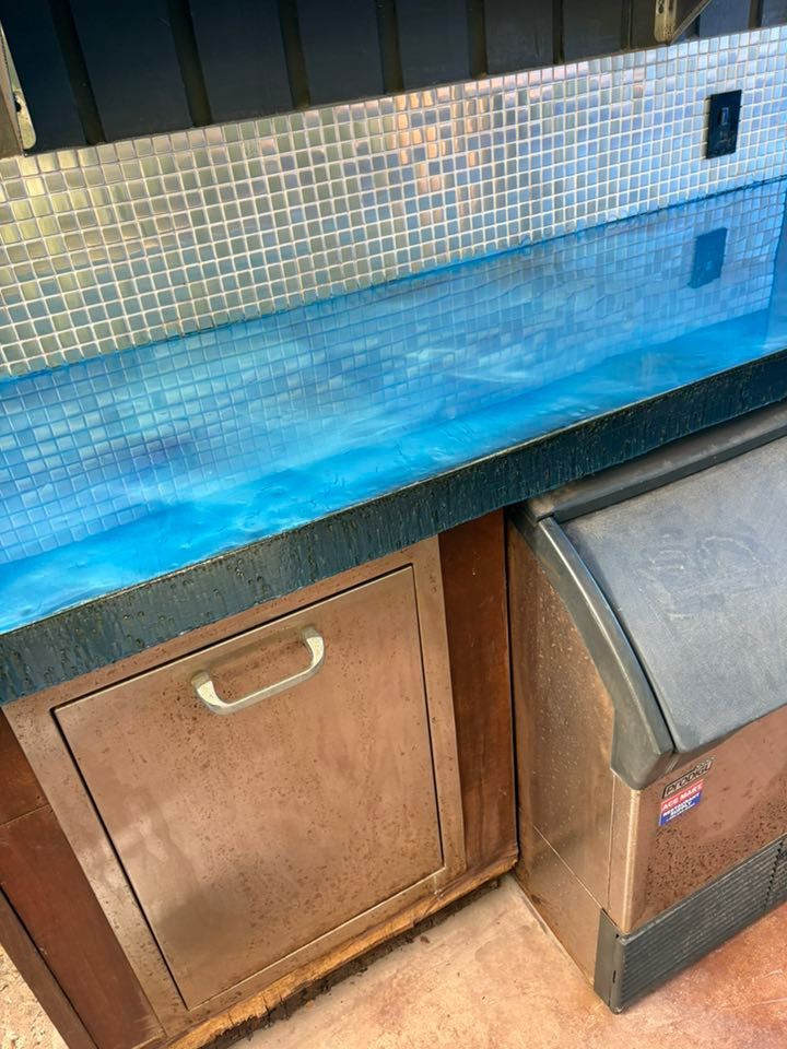 A bar area with a blue epoxy countertop and tile backsplash.  A stainless steel refrigerator and ice maker are visible.