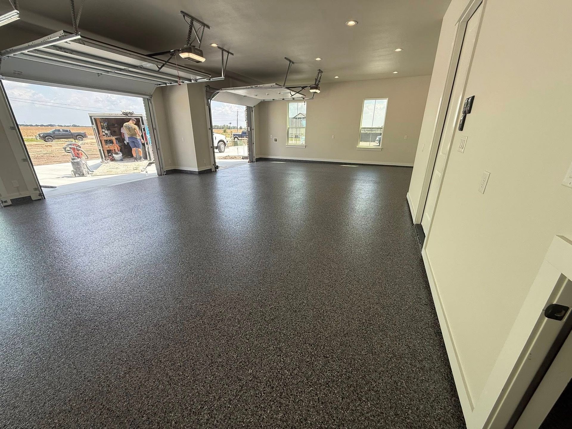Spacious garage with epoxy floor, open garage door, and white walls. Construction site visible outside.