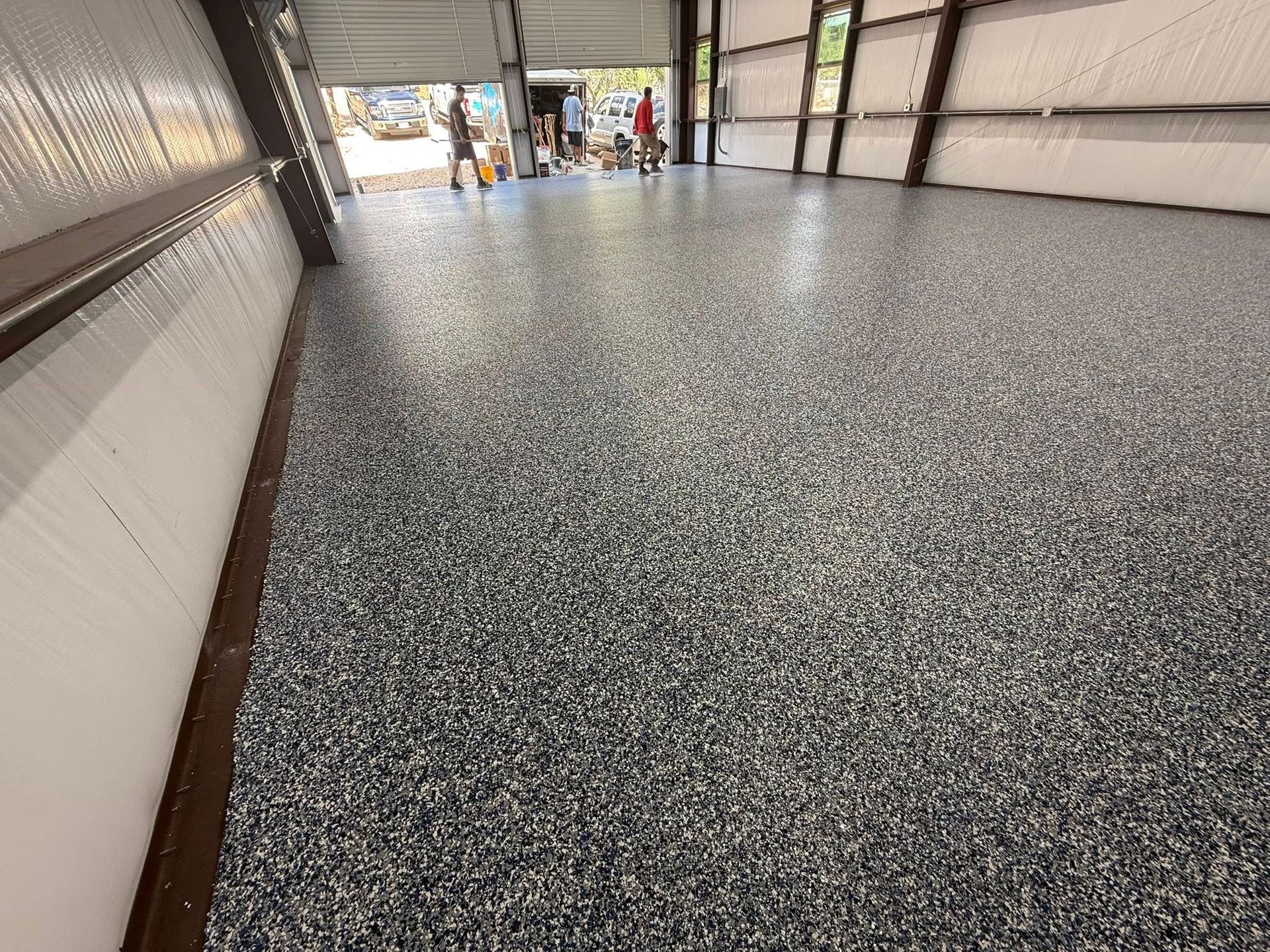 Epoxy-coated concrete floor, speckled with gray and blue chips, inside an open-air industrial building.