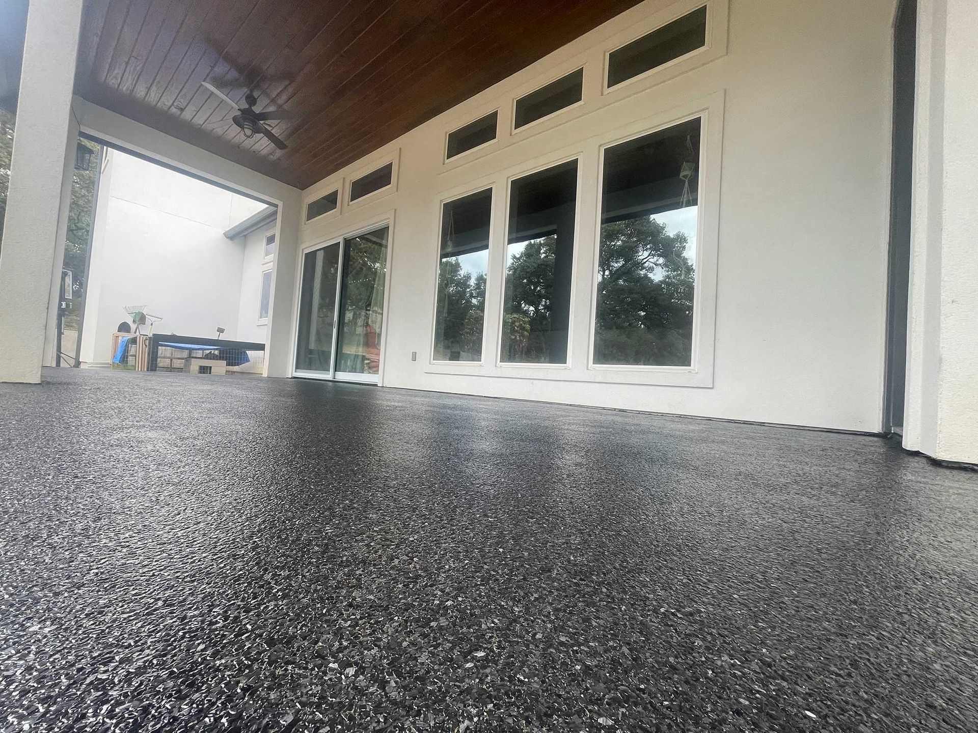 Dark, glossy patio floor with a covered porch. Glass doors and windows reflect the outdoors.