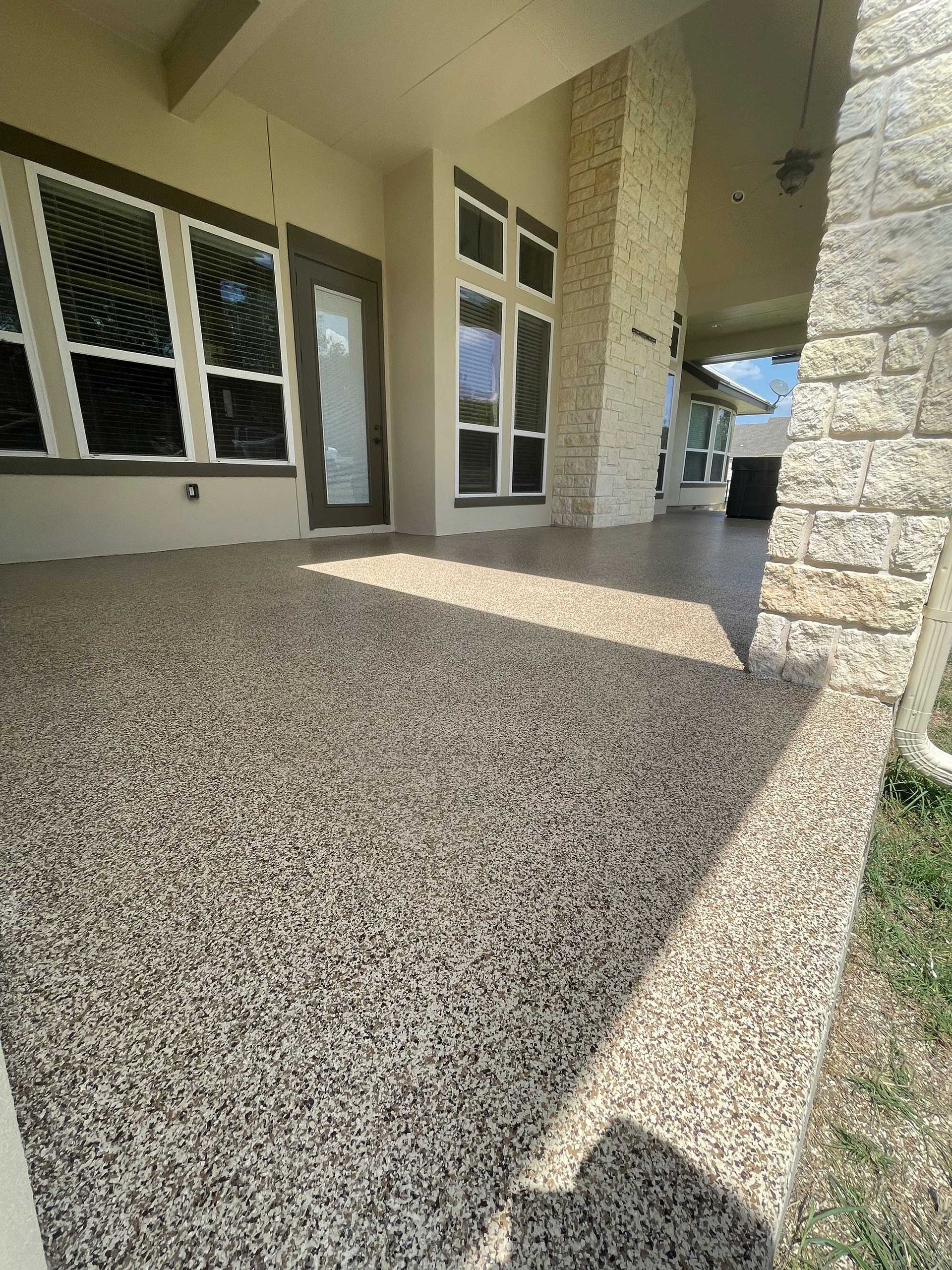 Covered patio with textured, speckled floor and stone columns.