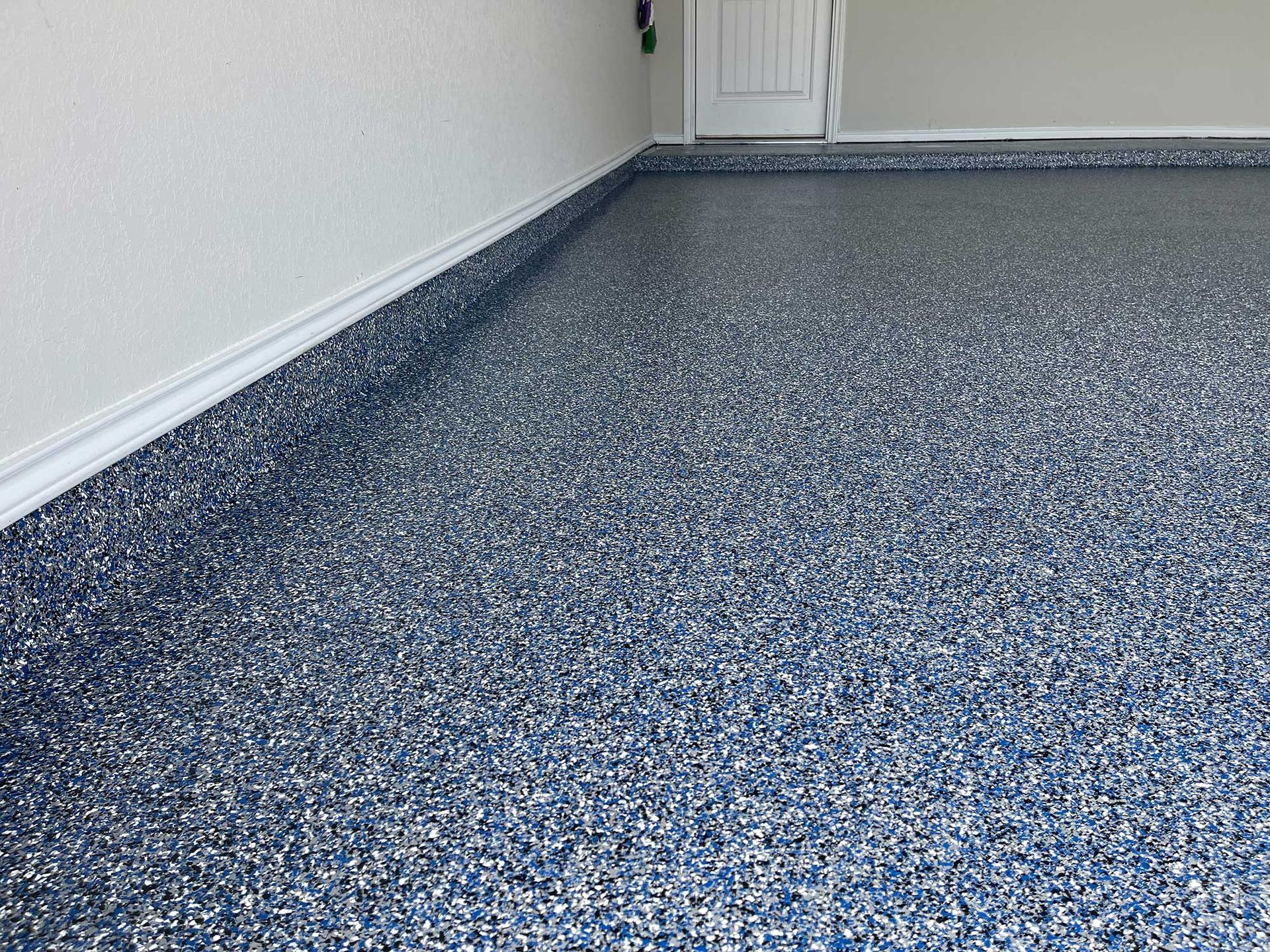 Epoxy garage floor with blue, white, and gray flakes. Corner of wall visible.