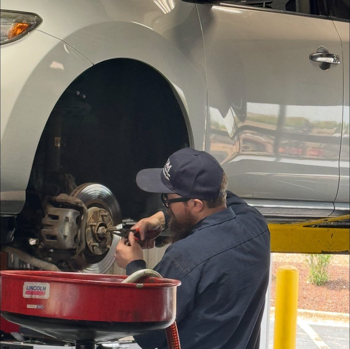 Mechanic working on a car's brakes at a shop, using tools. An oil pan is on the ground.