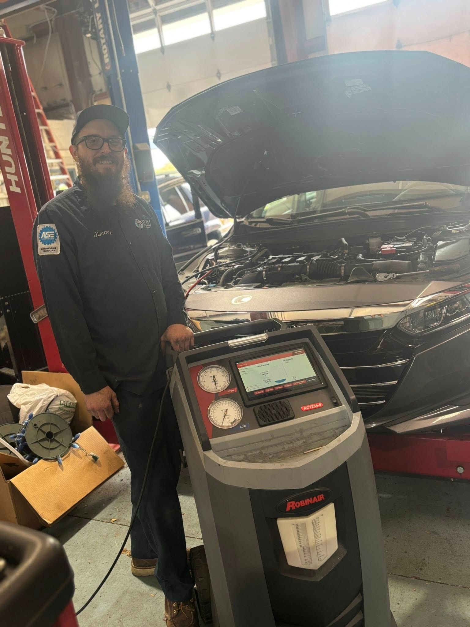 Mechanic next to an AC machine with car engine open.