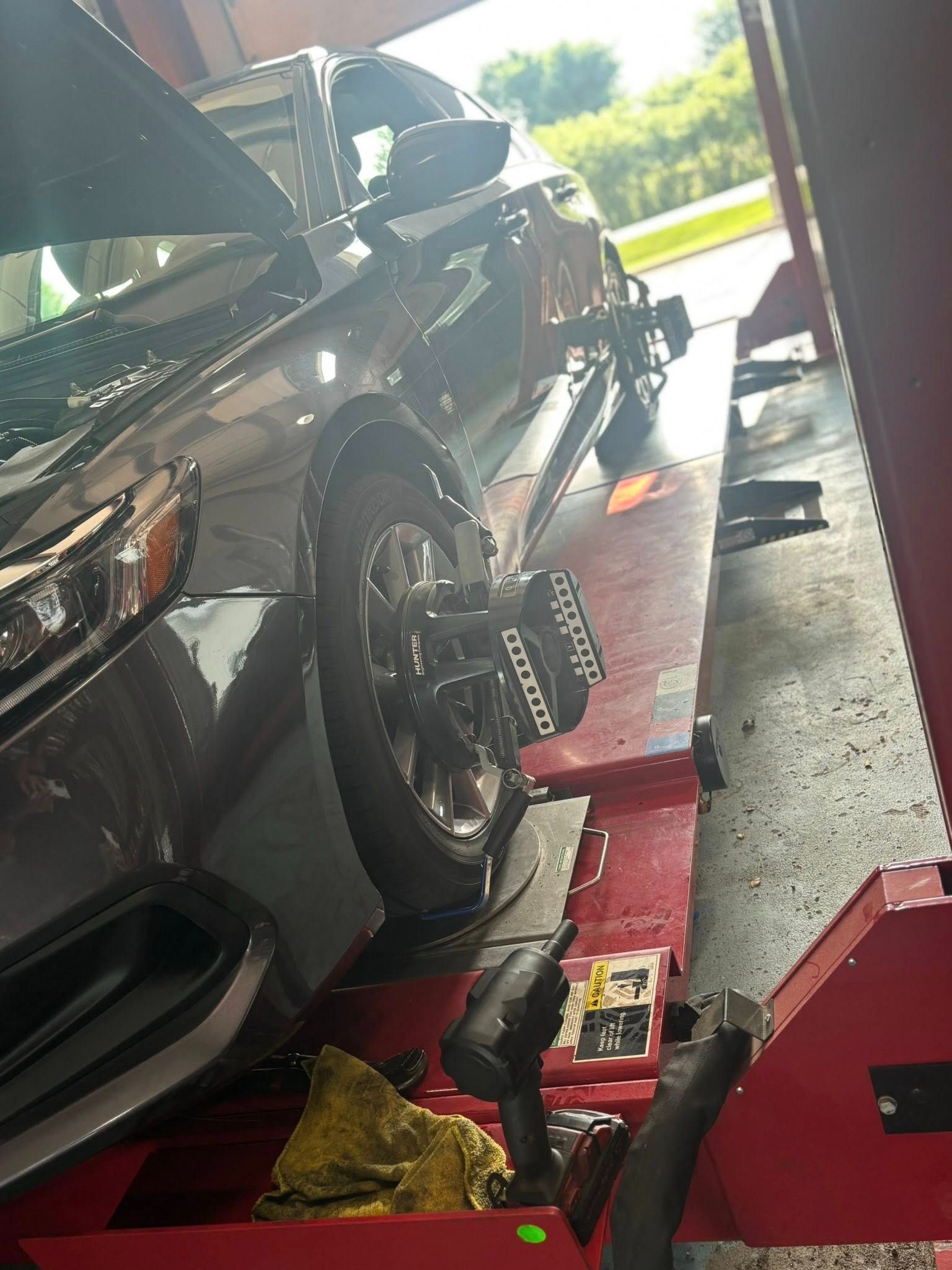 Car on a lift getting wheel alignment. Grey car with black wheels and a wrench.