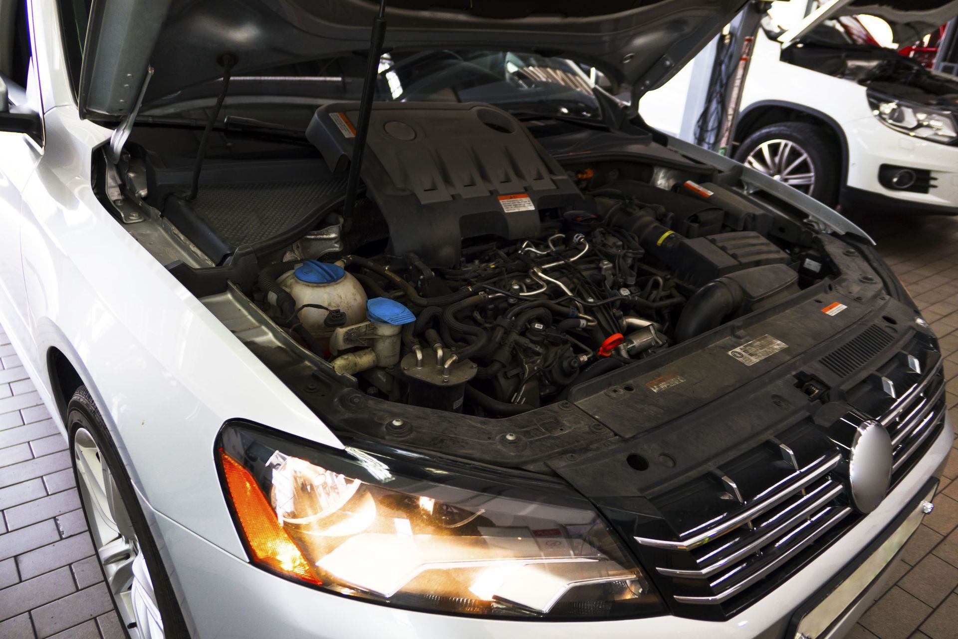 White car with hood open, exposing engine bay. Bright headlight illuminates the front.