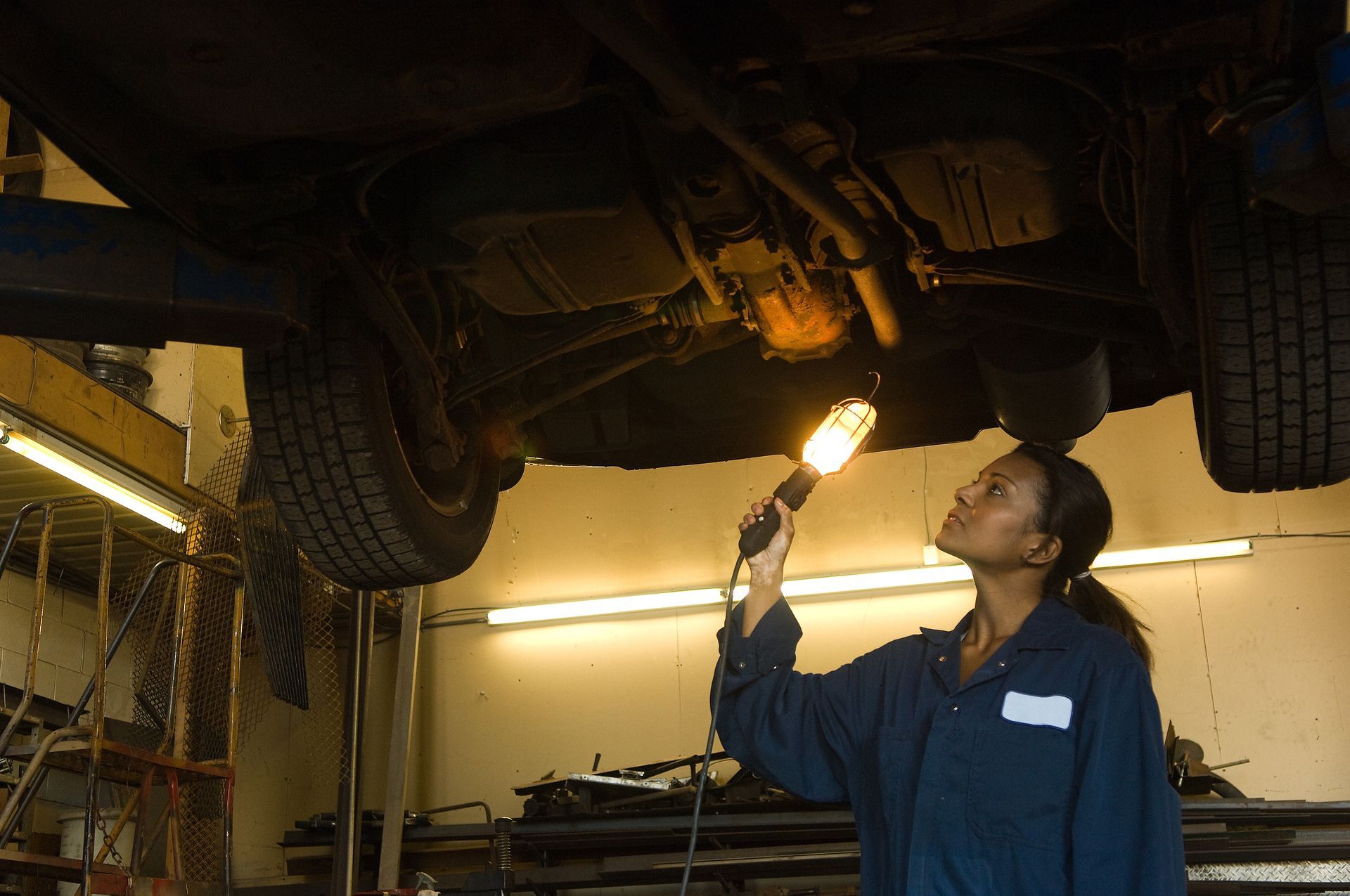 Mechanic inspecting undercarriage of vehicle with flashlight in garage.