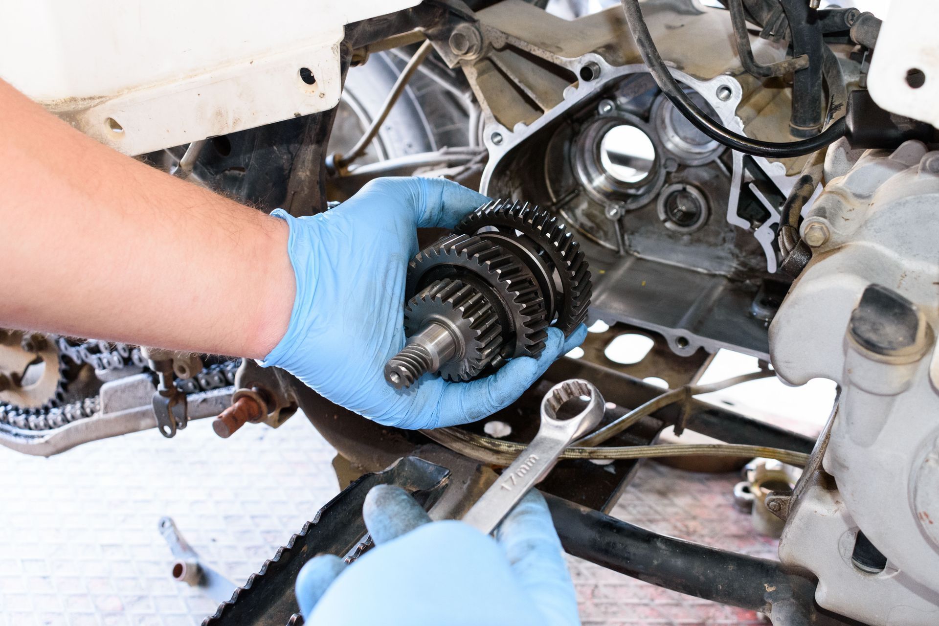 Hands in blue gloves holding gears, working on an ATV engine with a wrench.