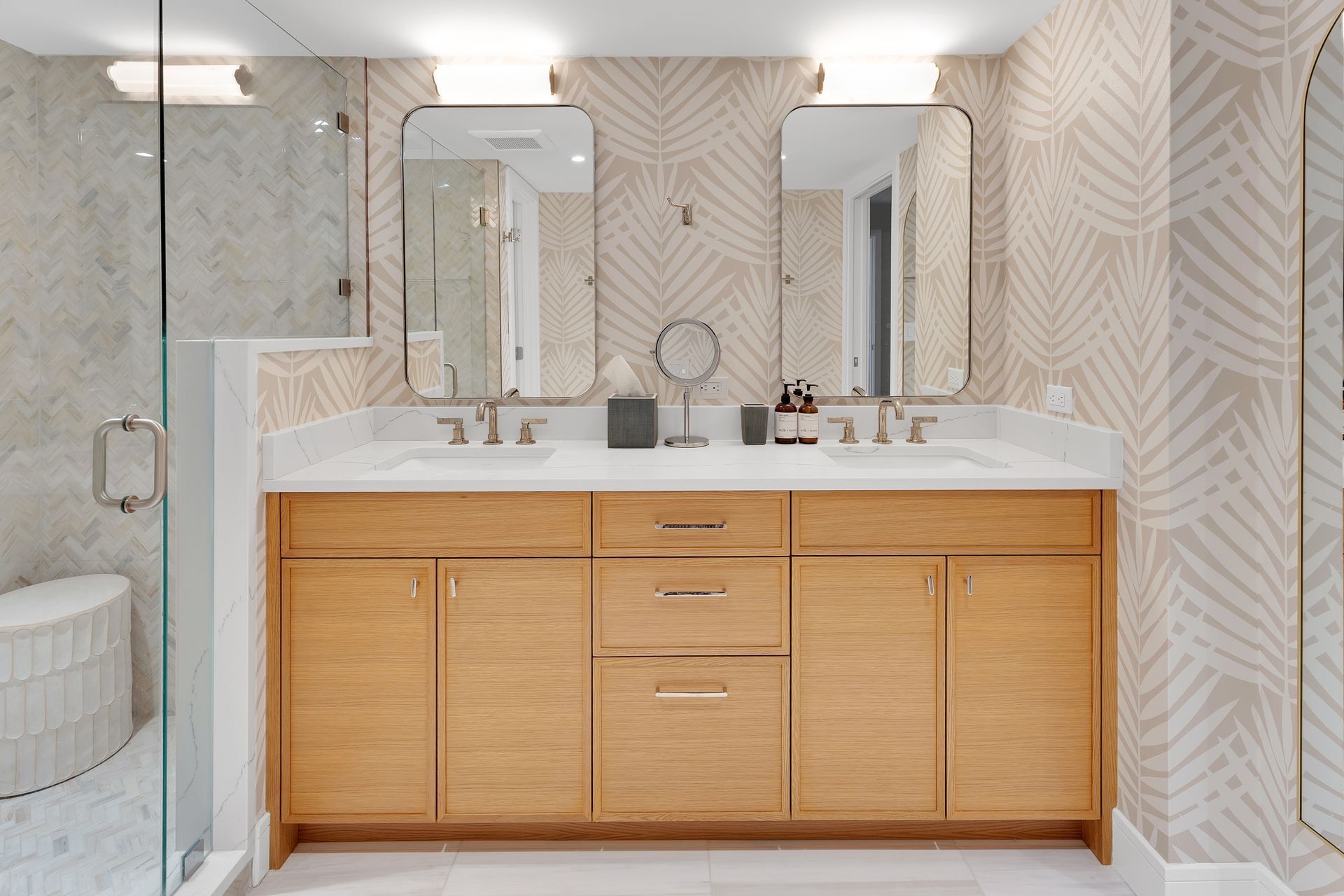 Modern bathroom vanity with wood cabinets, white countertop, mirrors, and beige patterned tile walls