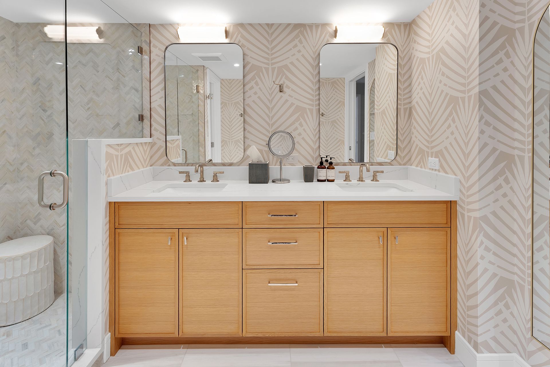Modern bathroom vanity with wood cabinets, large mirrors, and beige patterned tile walls.