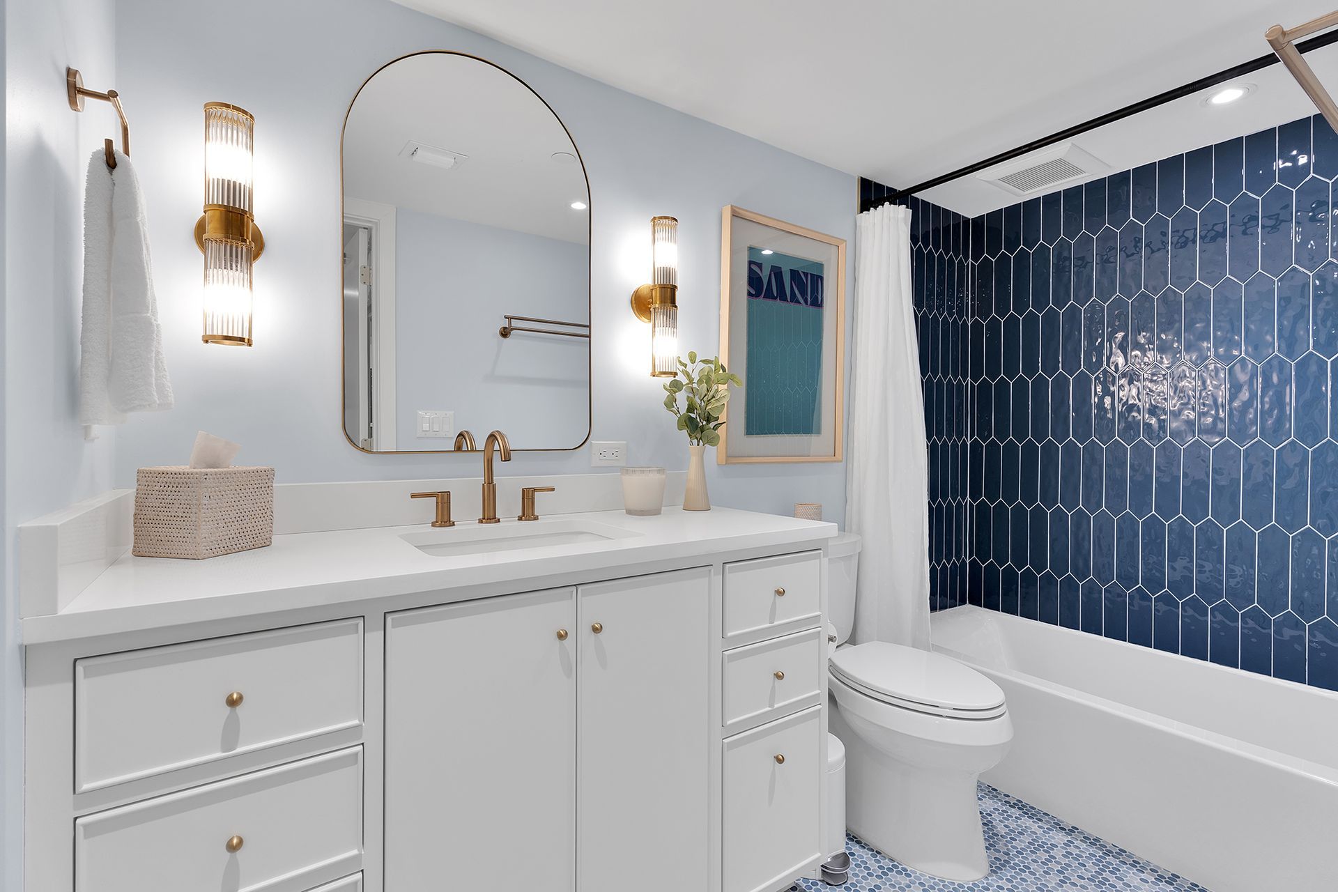 Bright white bathroom with gold fixtures, arched mirror, and navy shower curtain with white pattern
