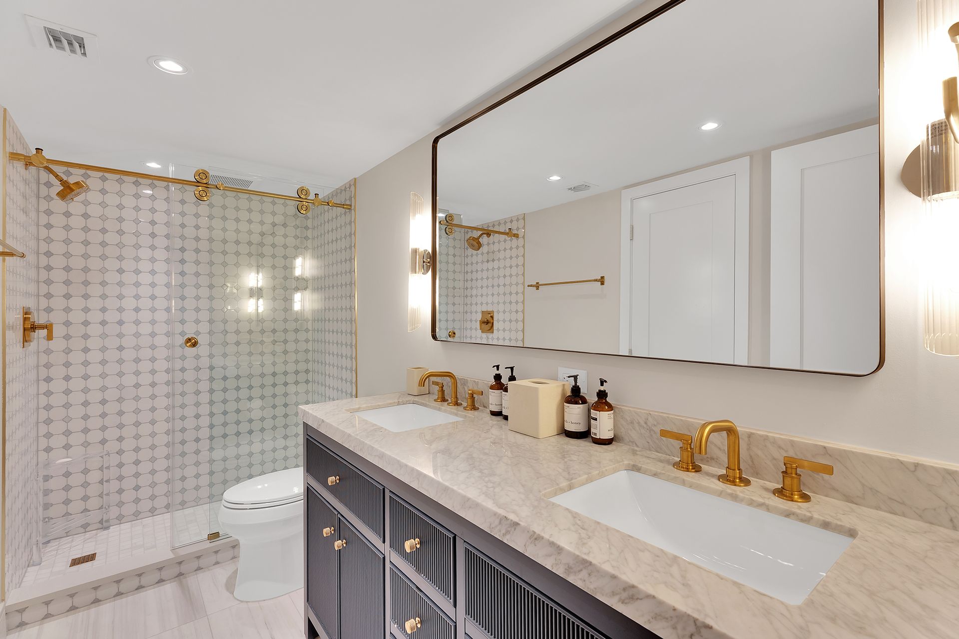 Bright bathroom with double vanity, gold fixtures, large mirror, and patterned shower curtain by the tub.