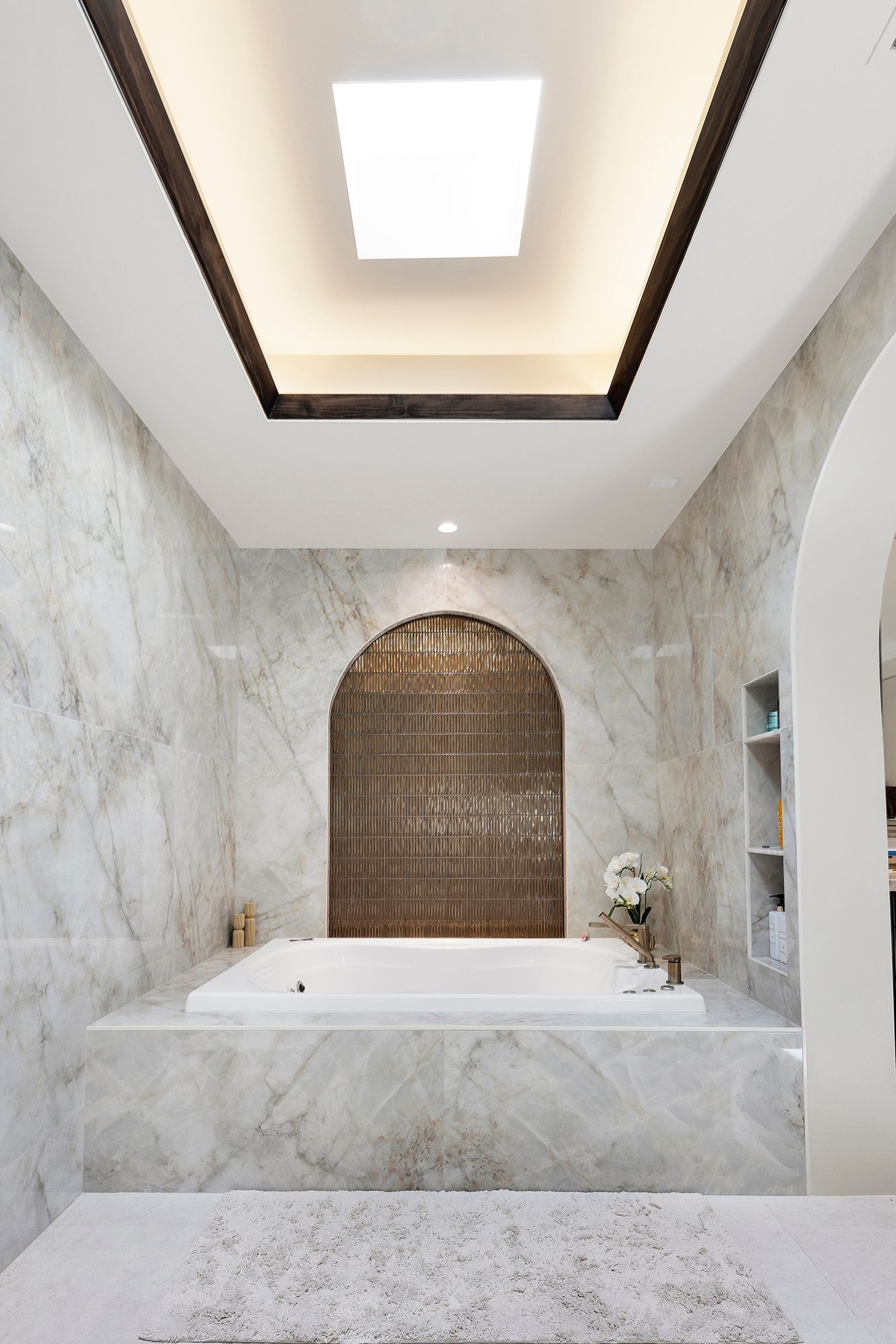 Modern marble bathroom with a freestanding tub, arched niche, and skylight ceiling