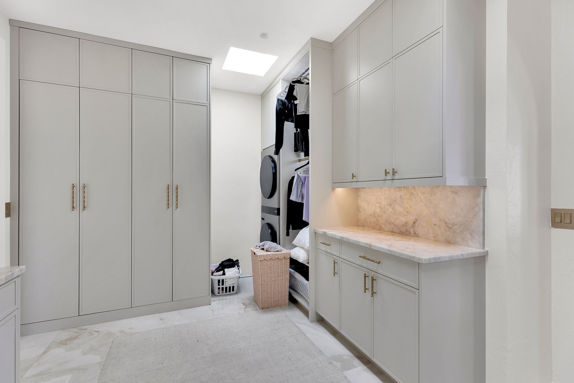 Bright laundry room with white cabinets, countertop, and stacked washer and dryer in the back.