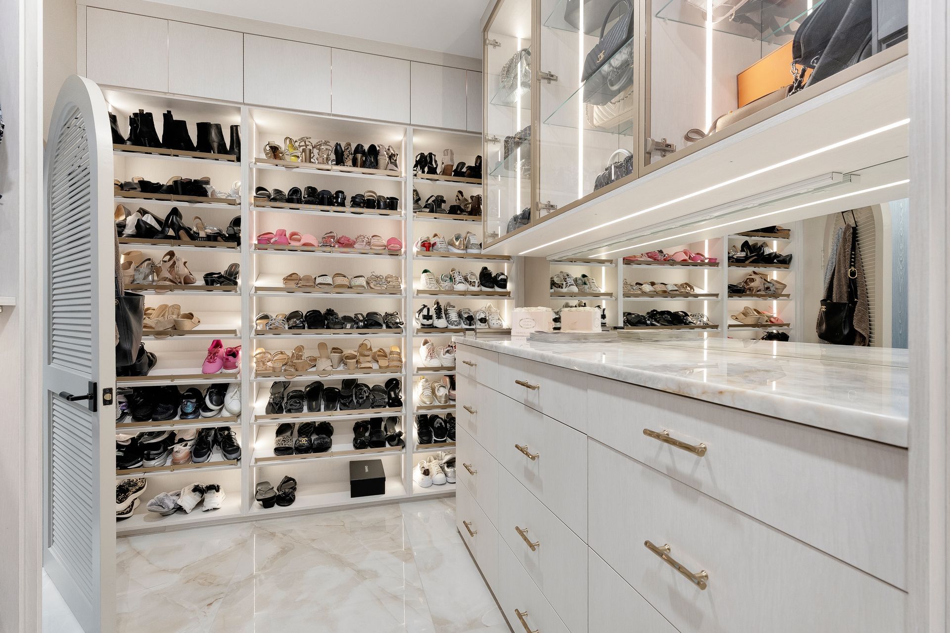 Luxurious walk-in closet with white cabinetry, marble floor, and shelves filled with shoes and handbags.