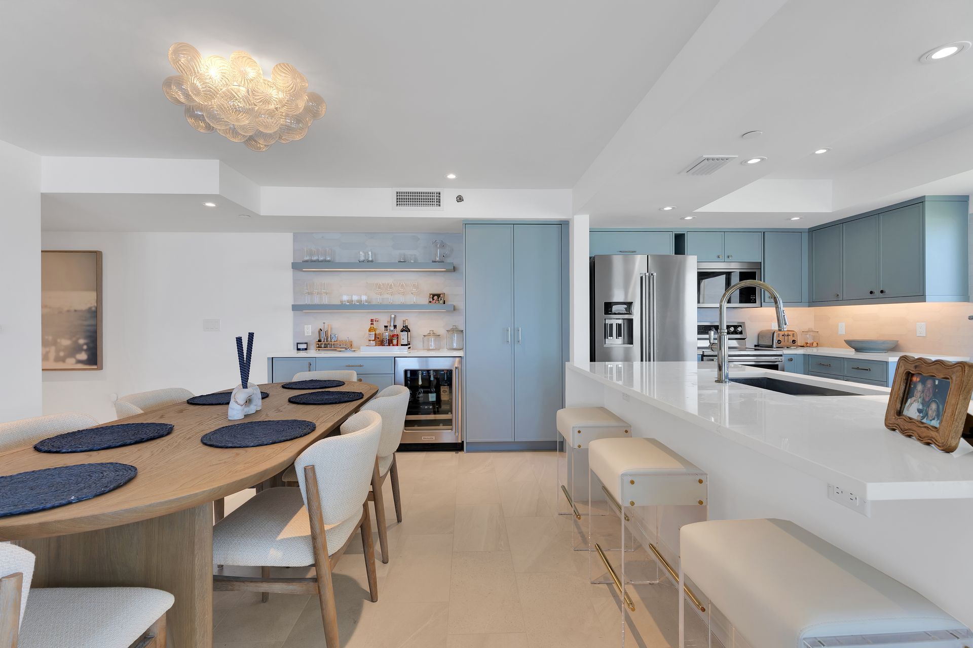 Bright modern kitchen and dining area with blue cabinets, white island, and wood table with chairs