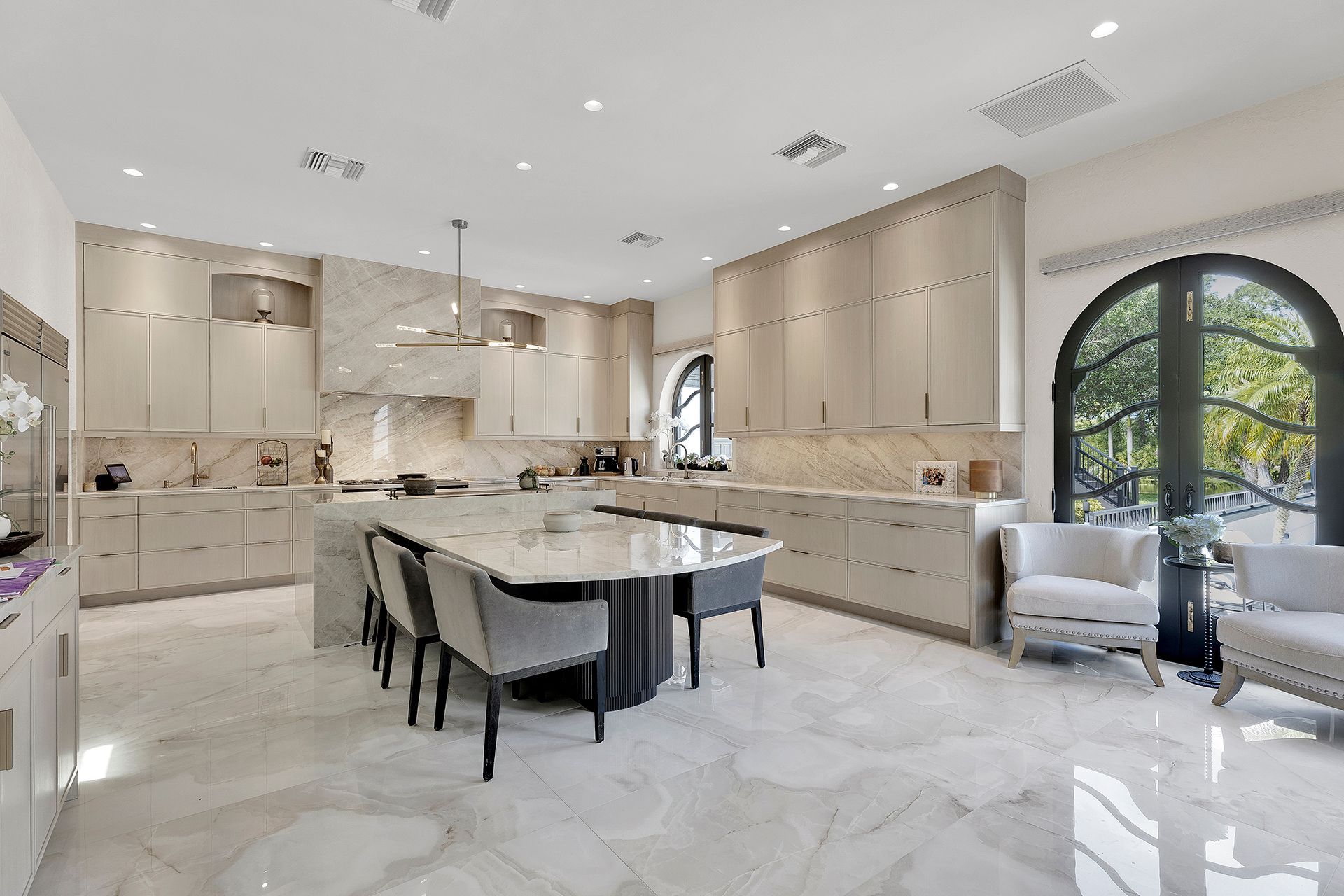 Bright modern kitchen with beige cabinets, marble island, and large arched window.