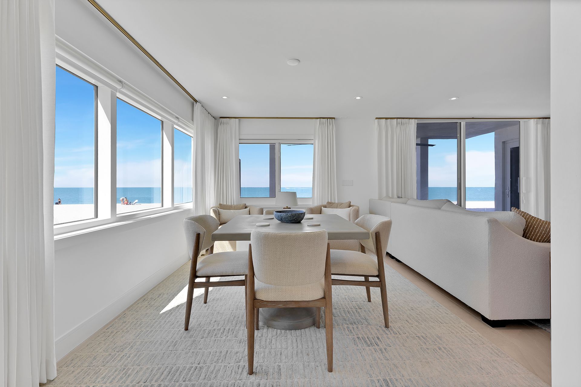 Bright beachside dining room with large windows, white furnishings, and ocean view