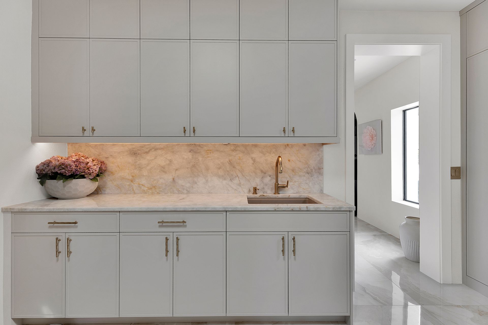 Modern white kitchen with gray cabinets, marble backsplash, and a small flower arrangement on the counter