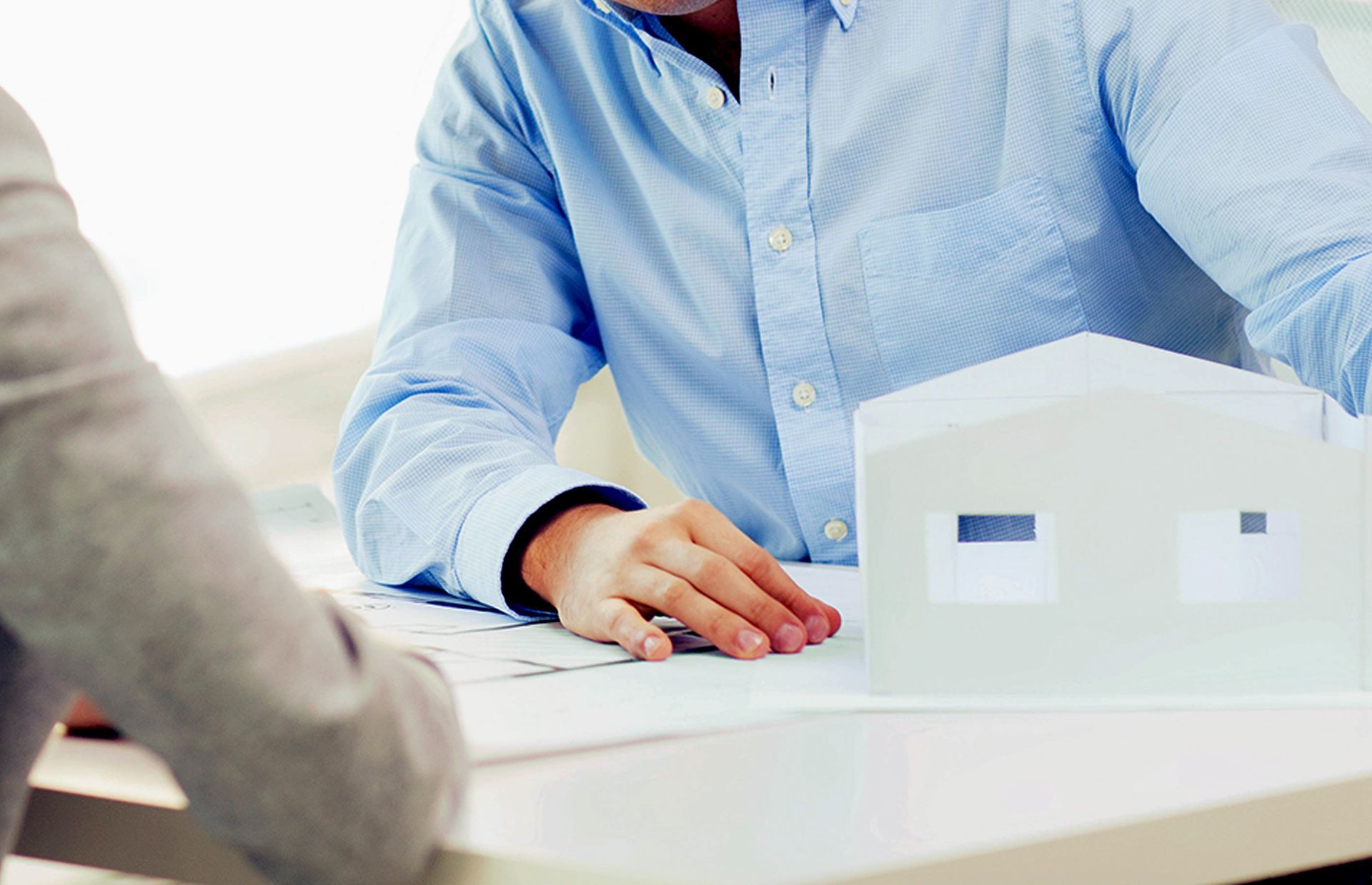 Two people discussing a white house model at a table, one in a light blue shirt.