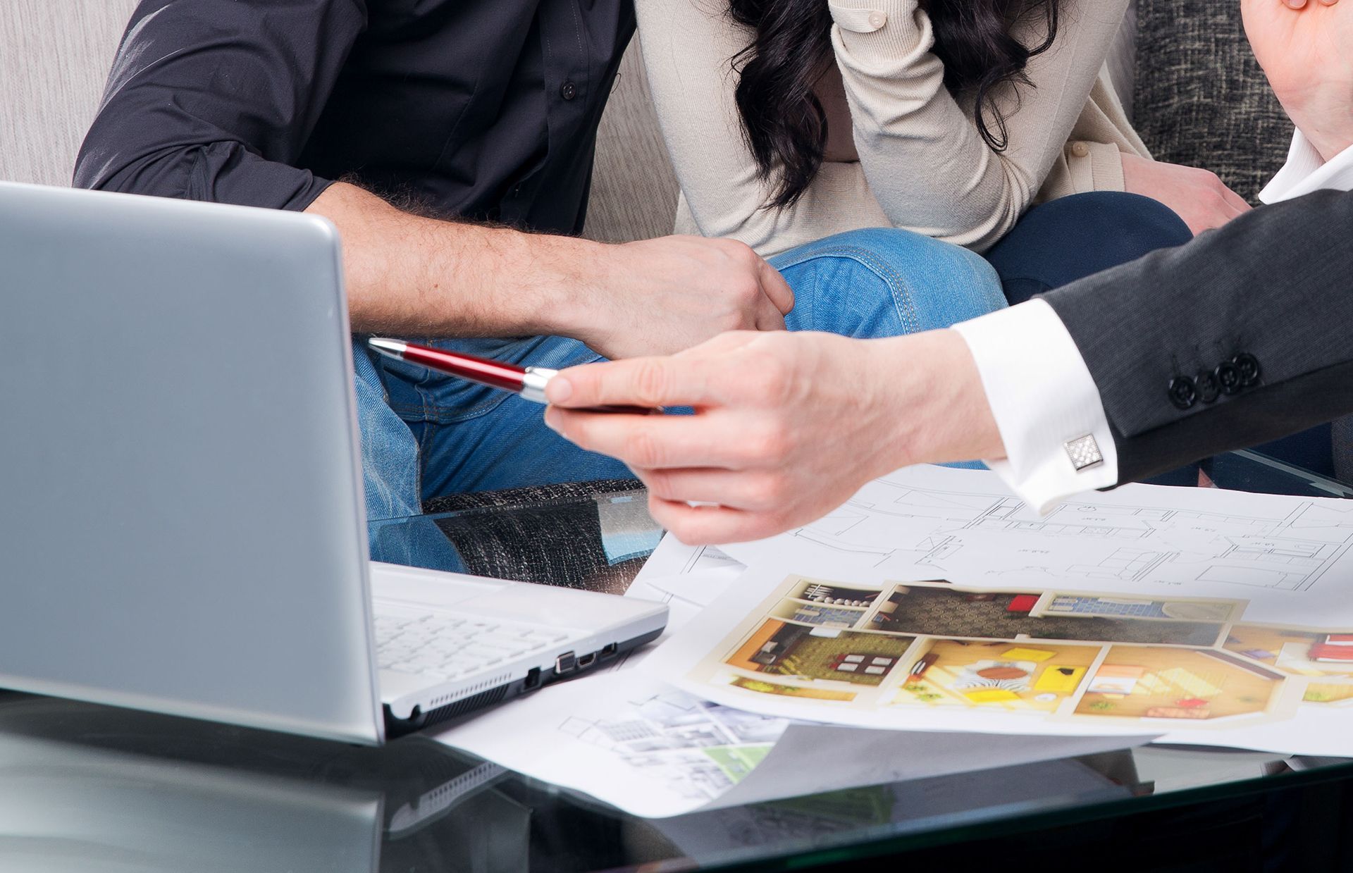 Colleagues reviewing documents at a laptop on a desk, with a pen pointing to printed photos.
