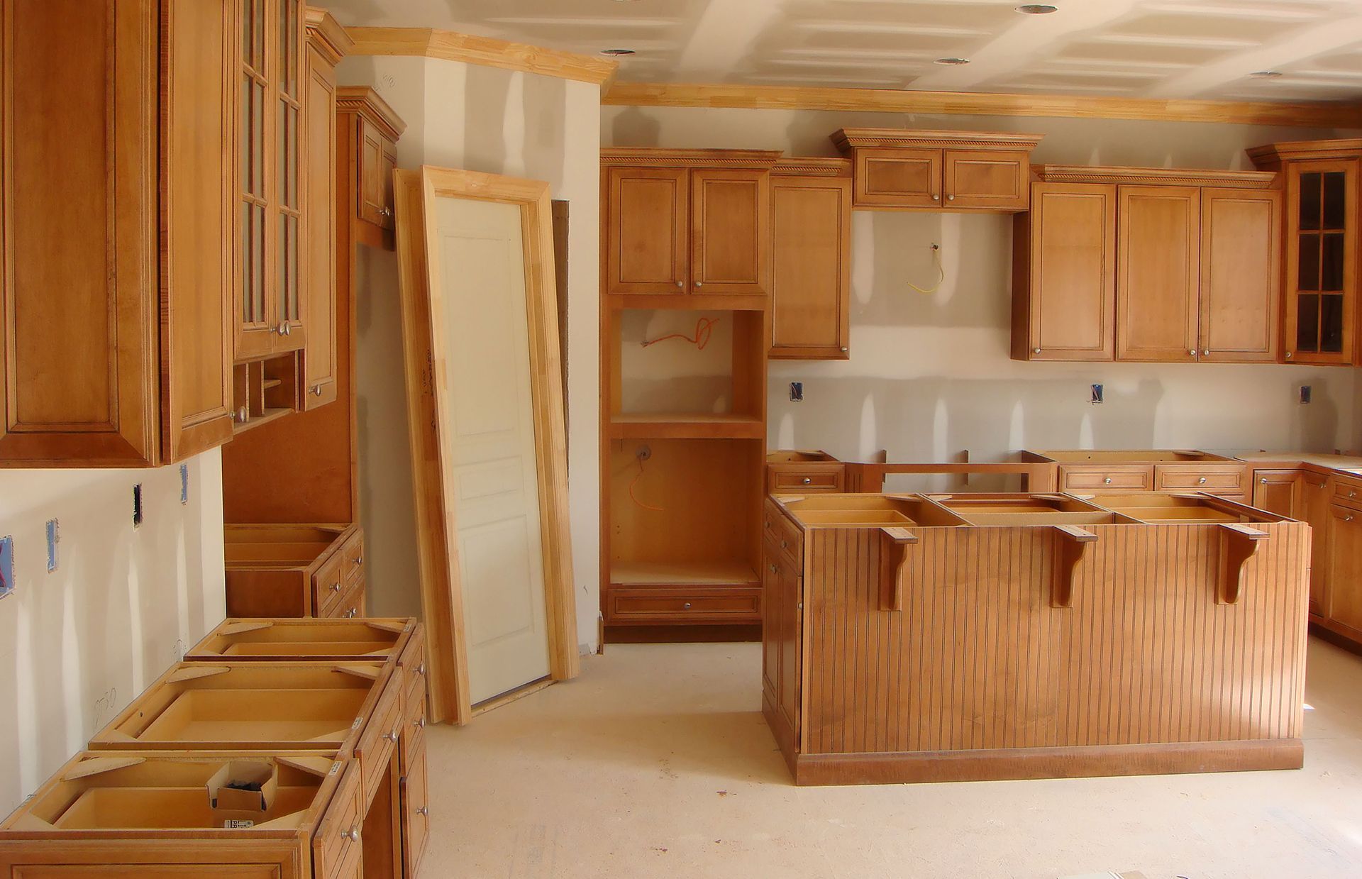Unfinished kitchen with wooden cabinets, island, and sink in a bright room under renovation