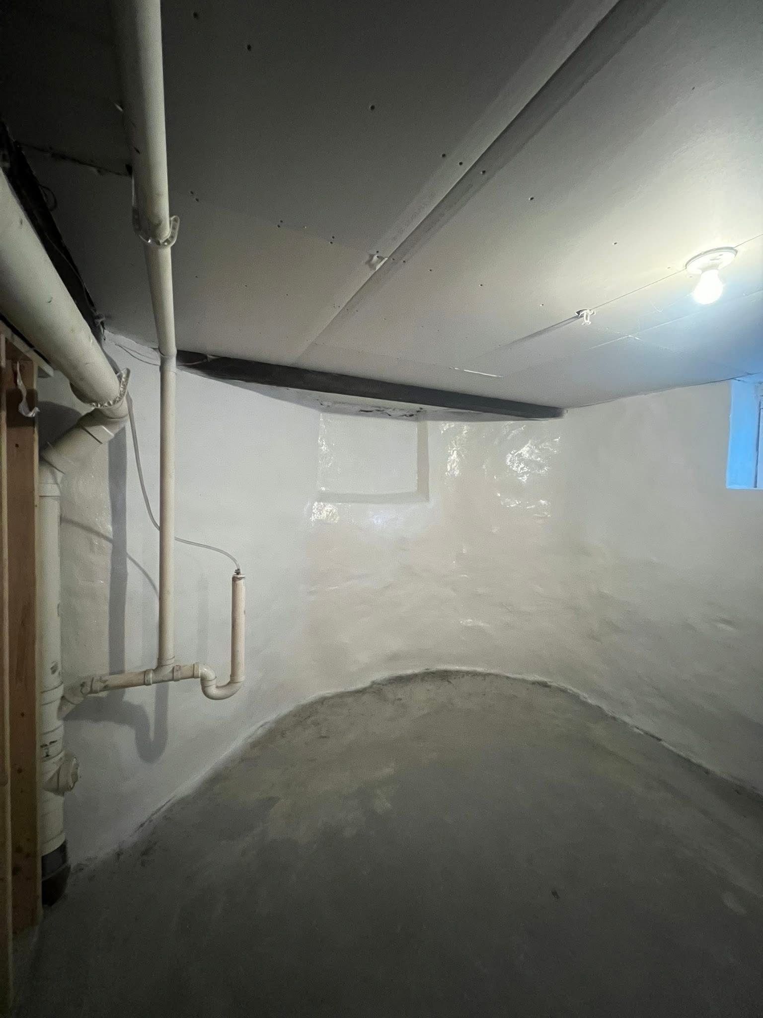 A white, curved basement room with concrete floor and exposed pipes on a wall.