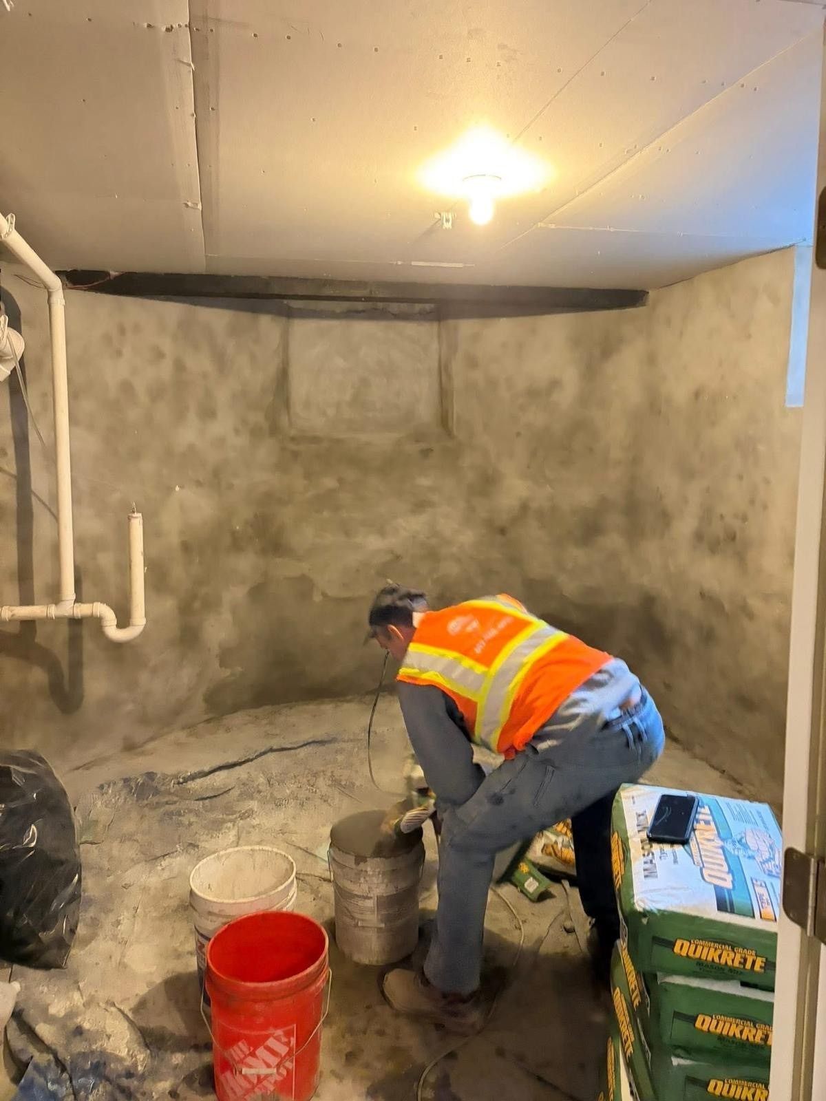Worker mixing cement in a basement. He is wearing a safety vest.