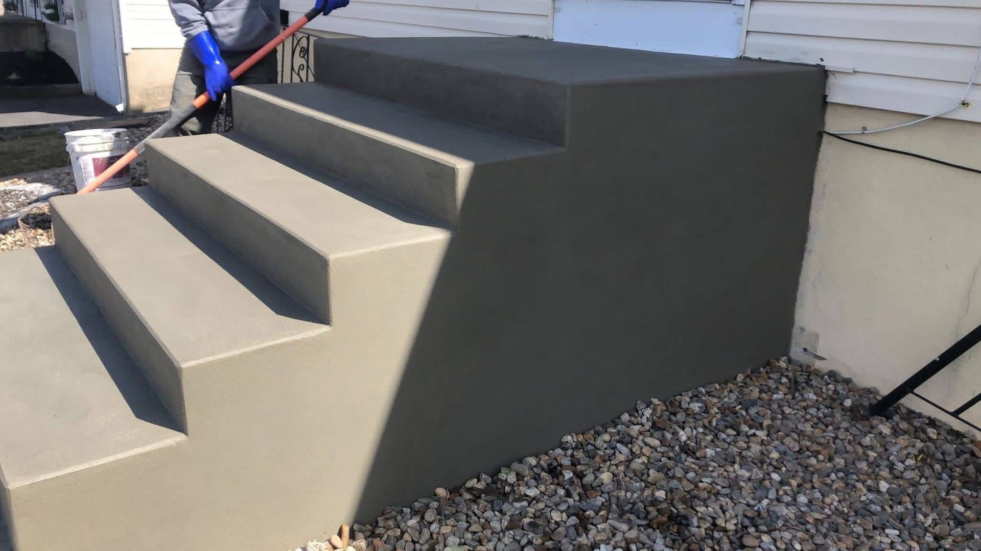 Person applying sealant to newly constructed concrete steps of a house.