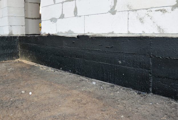 Black waterproof sealant applied to the foundation of a building made of white concrete blocks.