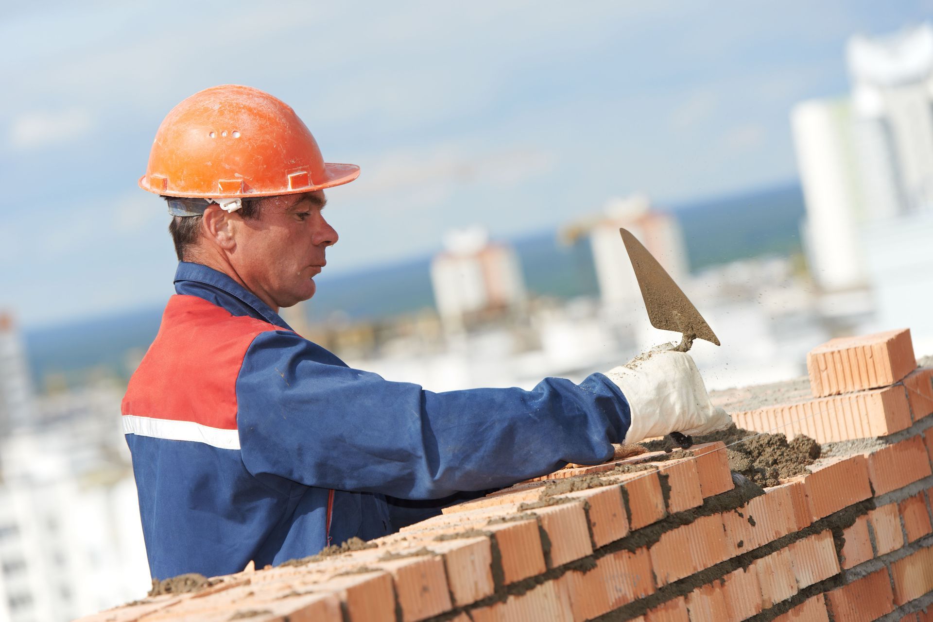 Construction worker in orange hard hat laying bricks on a rooftop with a trowel