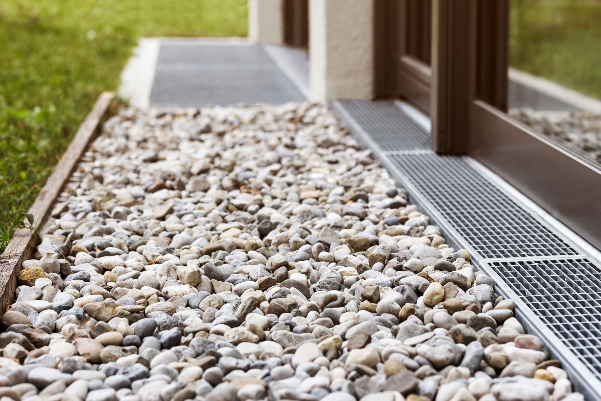 Gravel drainage bed beside a building with a metal grate and wooden posts