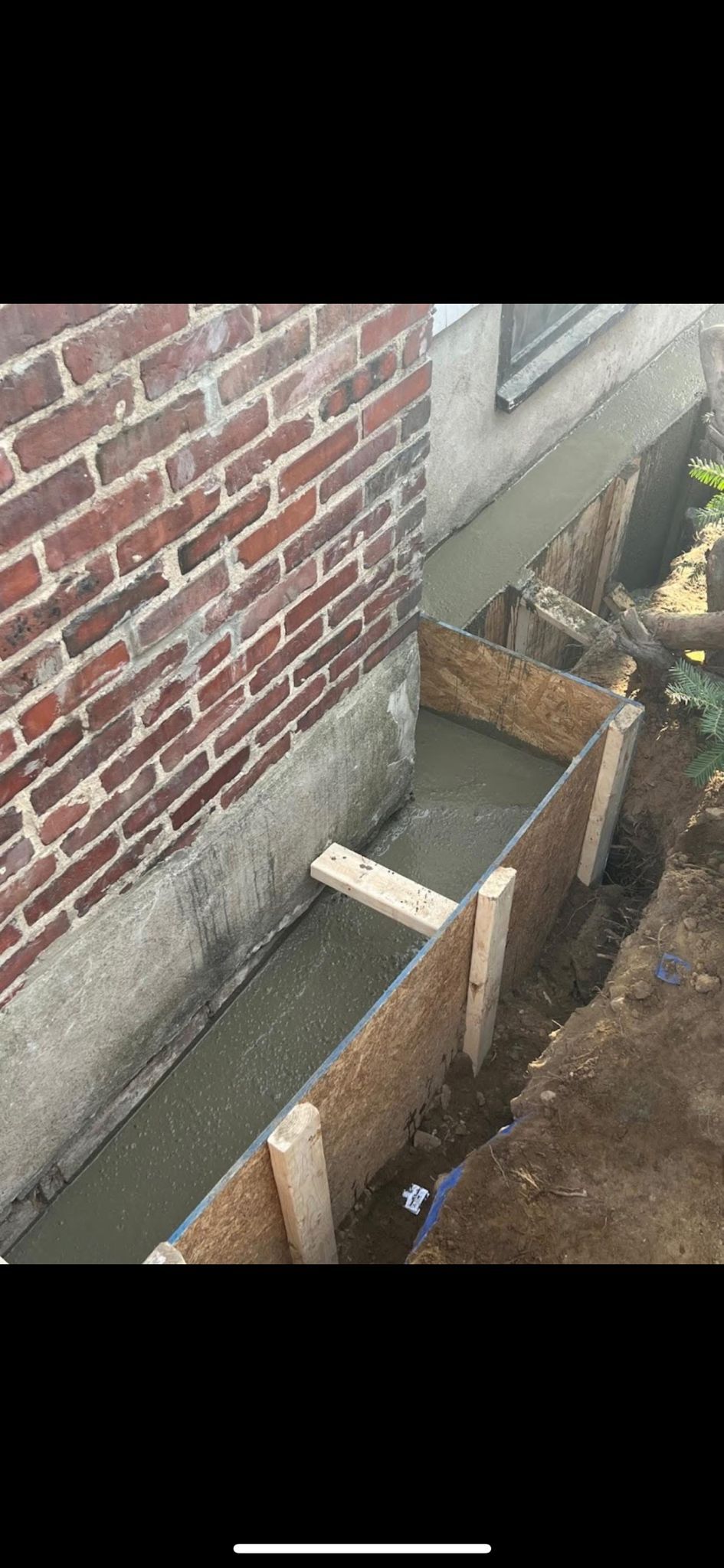 Brick house wall beside a narrow outdoor trench with concrete blocks and dirt