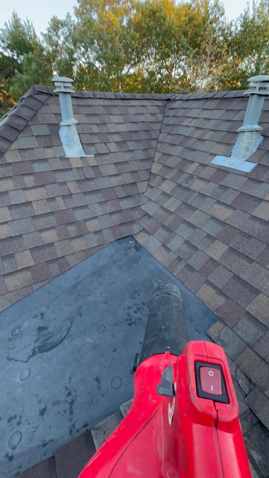Roof ridge and shingles with blue sealant patches, viewed from above; red tool visible at bottom.