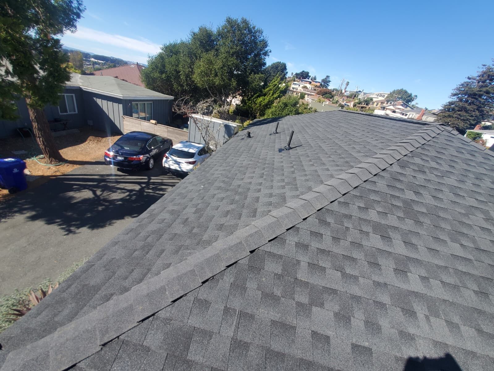 Roof shingles with a ridge vent, viewed from above, with a residential street and parked cars in the background