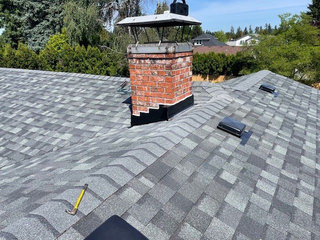 Gray shingled roof with a red brick chimney and a yellow utility knife near the ridge