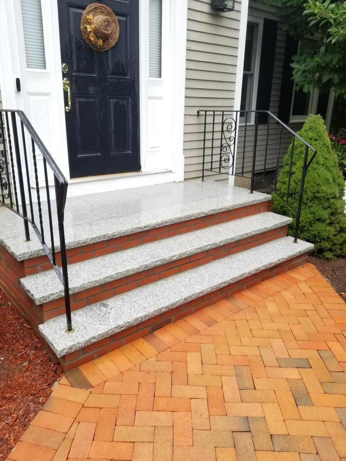 Front porch with black door, brick steps, white railings, and orange herringbone brick walkway.