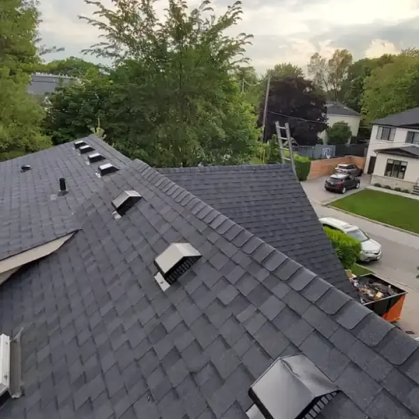 Dark gray shingled roof with skylights overlooking a residential neighborhood at dusk
