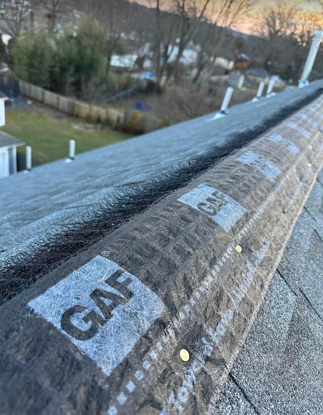 Roof edge with underlayment and “GAF” label, overlooking a yard and trees.