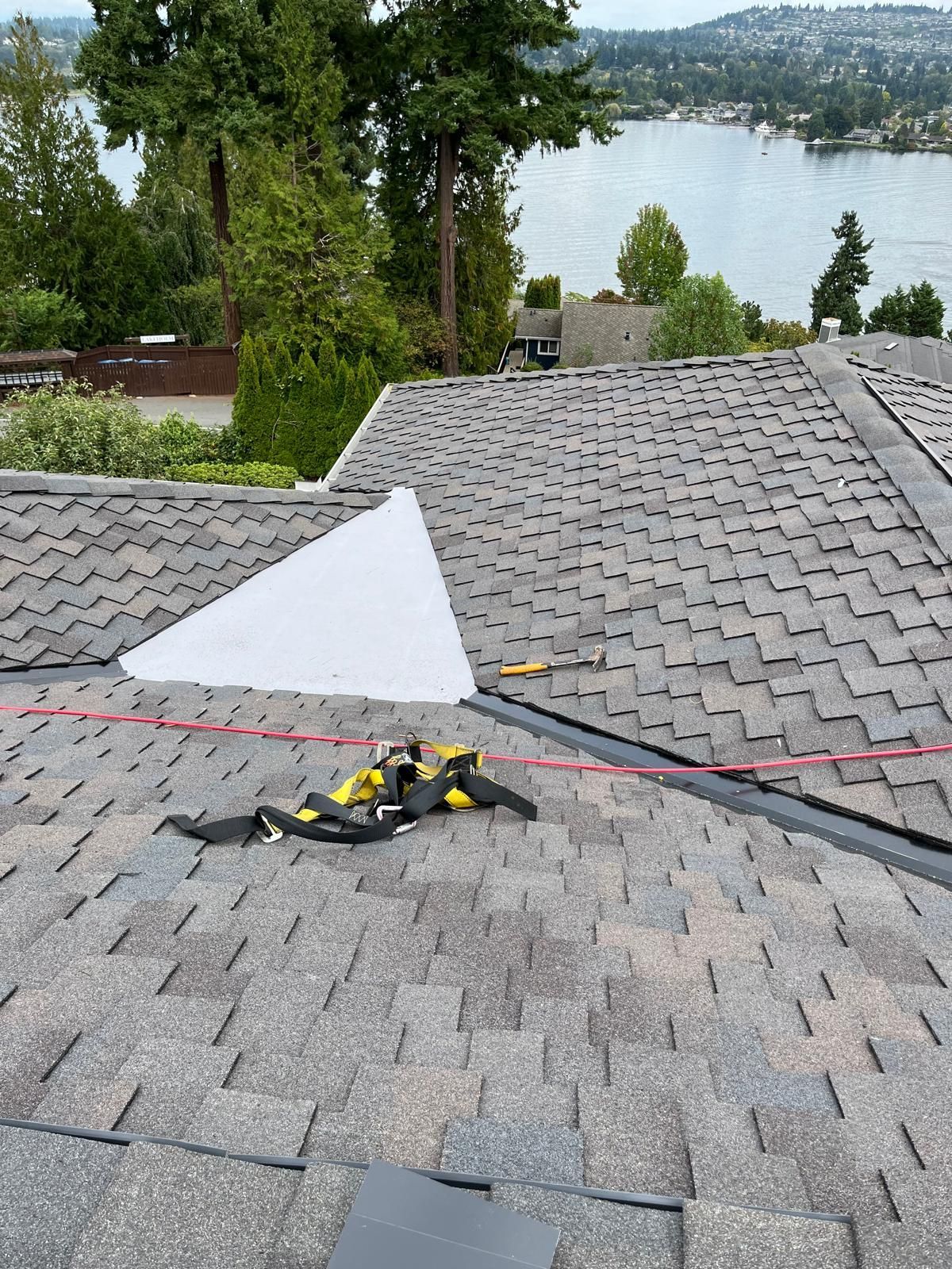 Rooftop with gray shingles, tools and cords, overlooking a lake and trees.