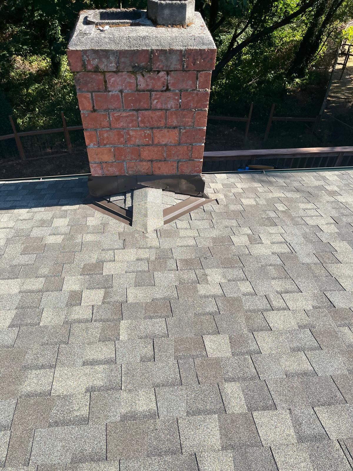 Brick chimney on a shingled roof with trees in the background