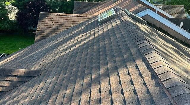 Brown shingle roof viewed from above with a skylight and sunlight casting diagonal shadows