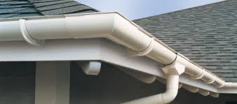 White rain gutters and downspouts along a gray shingled house roof corner